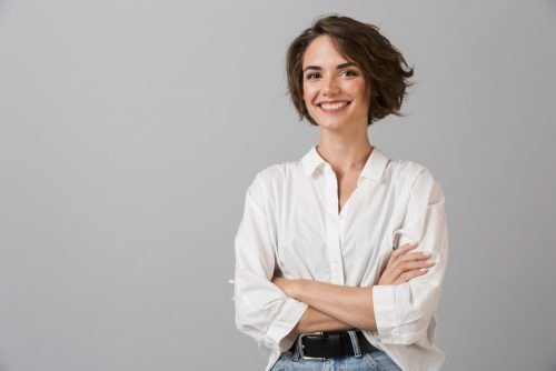 Confident woman in a soft-lit studio wearing a fitted blouse, showcasing natural, balanced proportions after breast augmentation