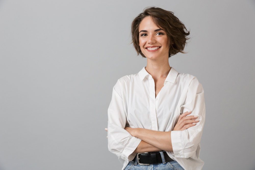 Confident woman in a soft-lit studio wearing a fitted blouse, showcasing natural, balanced proportions after breast augmentation